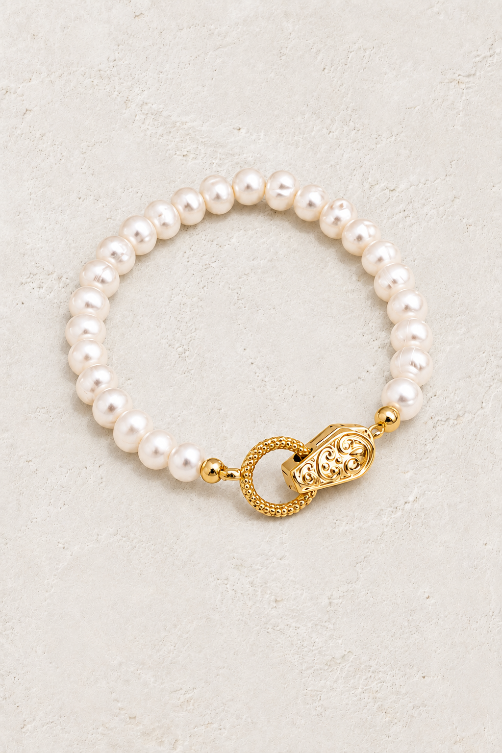 
                  
                    Eternal Pearl bracelet with ornate gold clasp on a warm off-white textured plaster background
                  
                