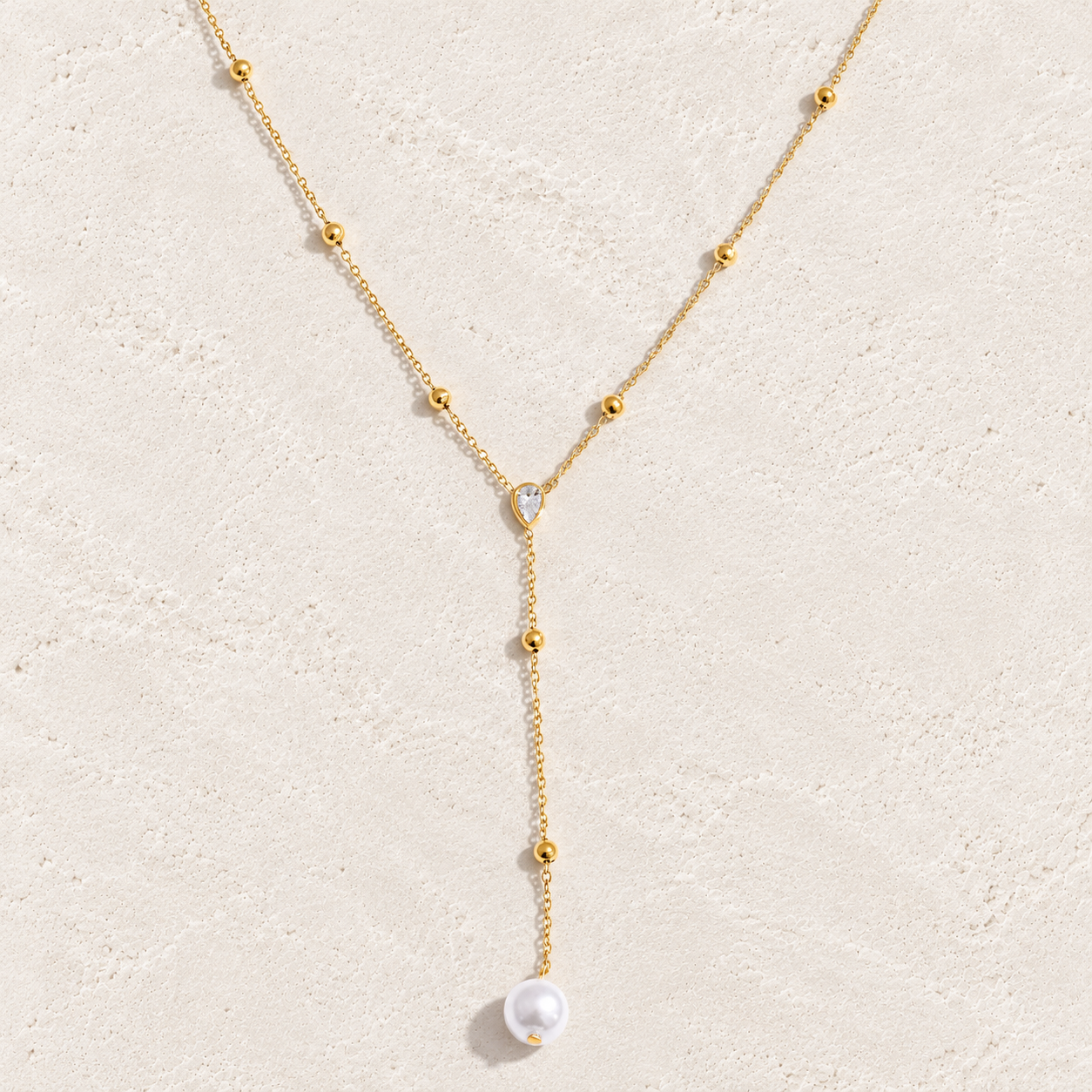
                  
                    Gold pearl and crystal lariat necklace on cream stone
                  
                