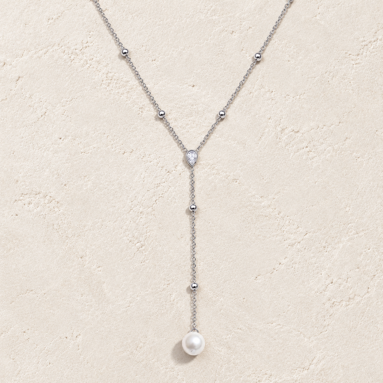 
                  
                    Silver pearl and crystal lariat necklace on cream stone
                  
                