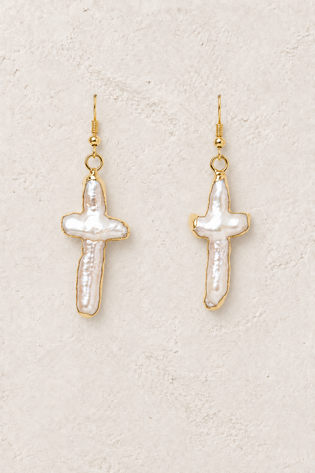 Faith freshwater pearl cross drop earrings on a warm off-white textured background