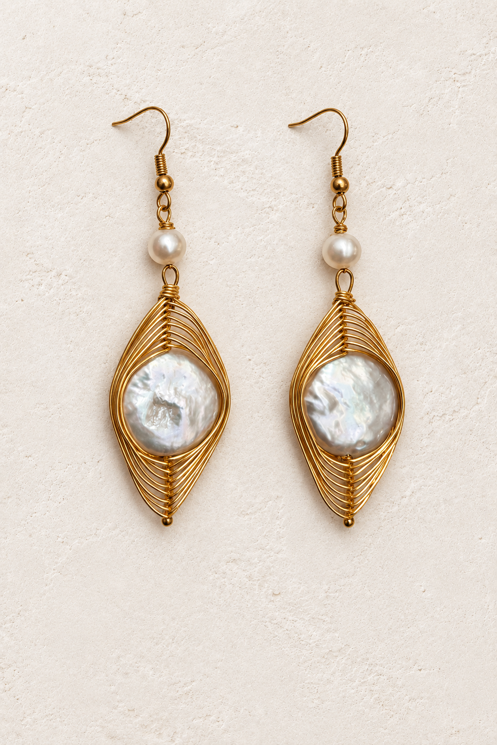Fiora Gold Wire Wrapped Pearl Earrings on cream plaster background