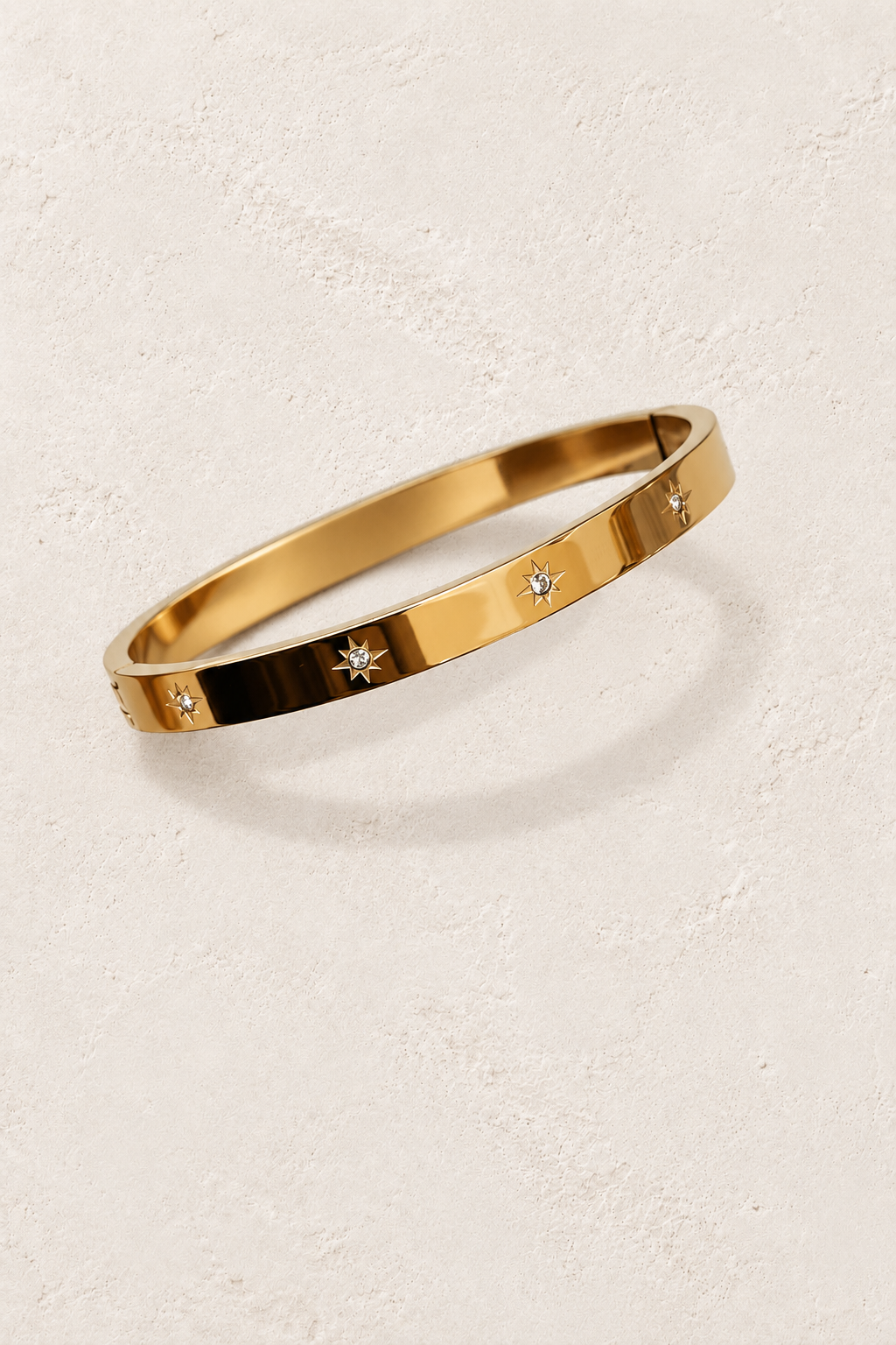 Forelle Gold Starlight Bangle on cream beige textured background