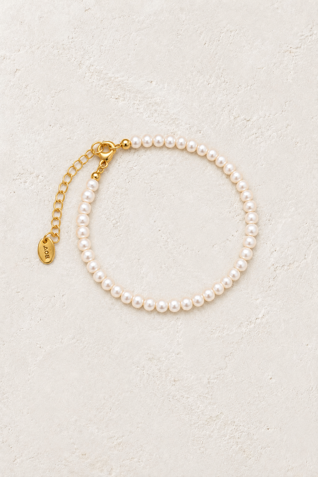 Freshwater pearl and gold bead bracelet on a warm off-white textured plaster background