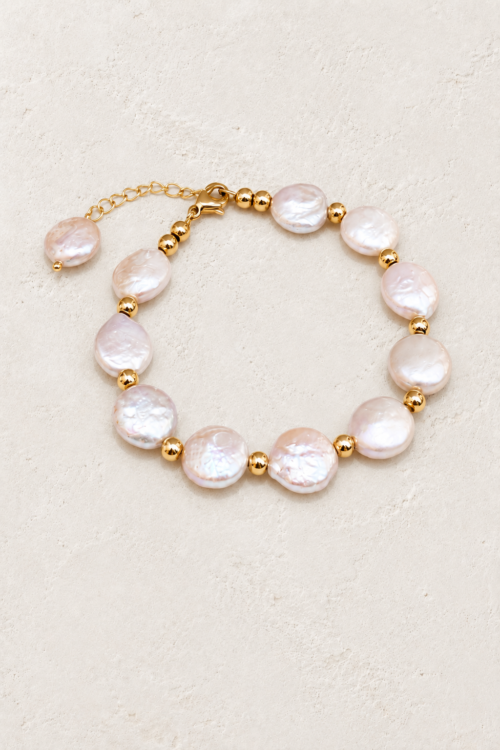 Freshwater pearl coin bracelet with gold beads on a warm off-white textured plaster background