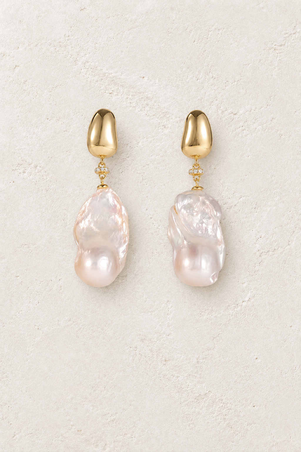 Gold plated baroque freshwater pearl drop earrings on a warm off-white textured plaster background
