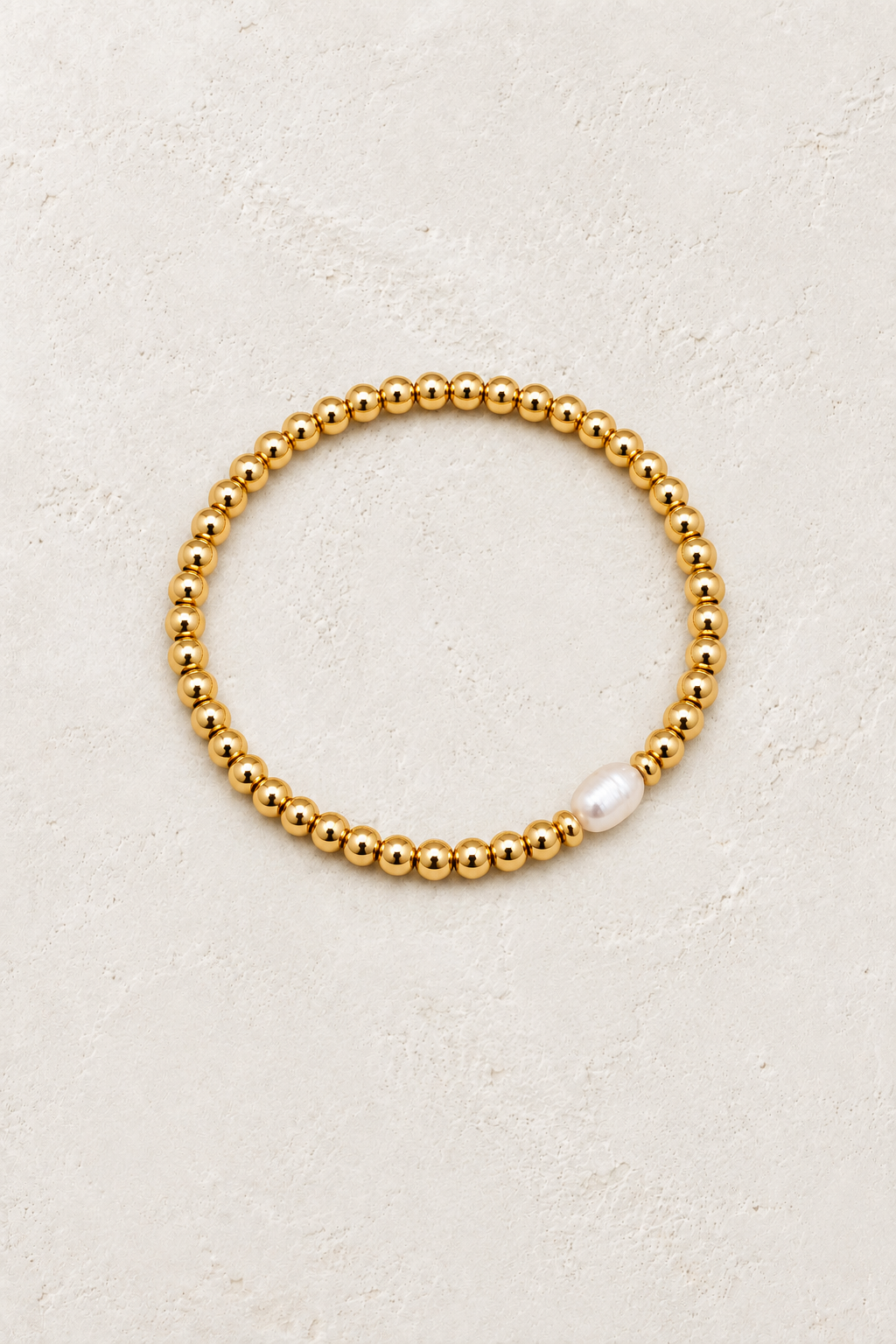 Polished gold bead bracelet on a warm off-white textured plaster background