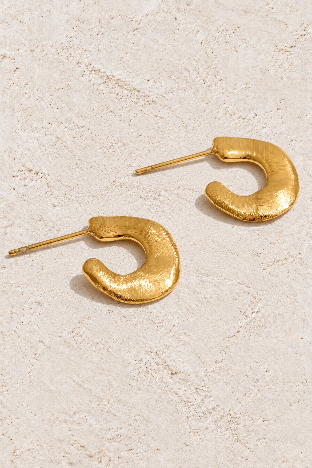 
                  
                    Gold brushed mini hoop earrings on cream plaster
                  
                