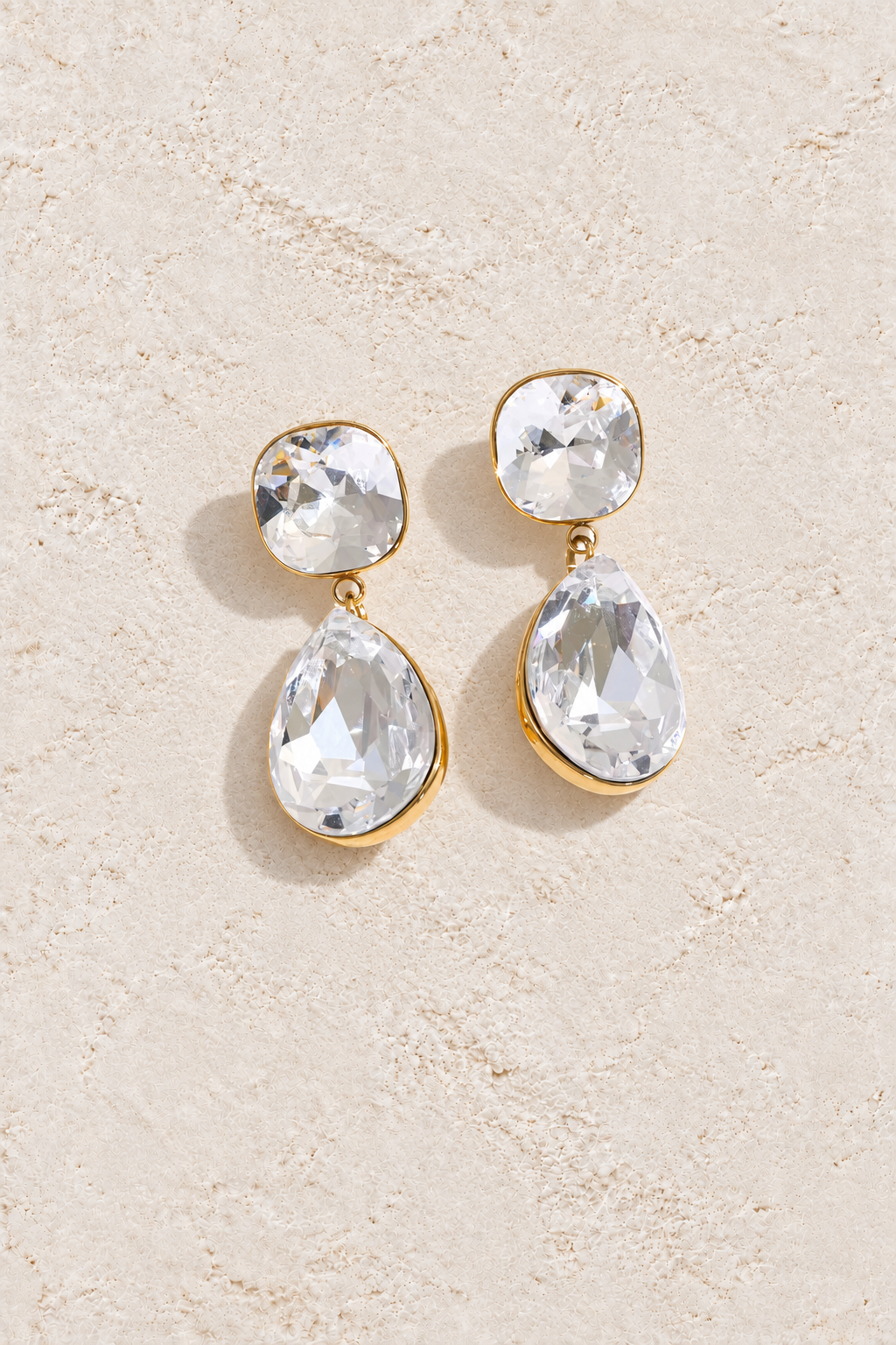 Gold cushion and pear crystal drop earrings on cream plaster