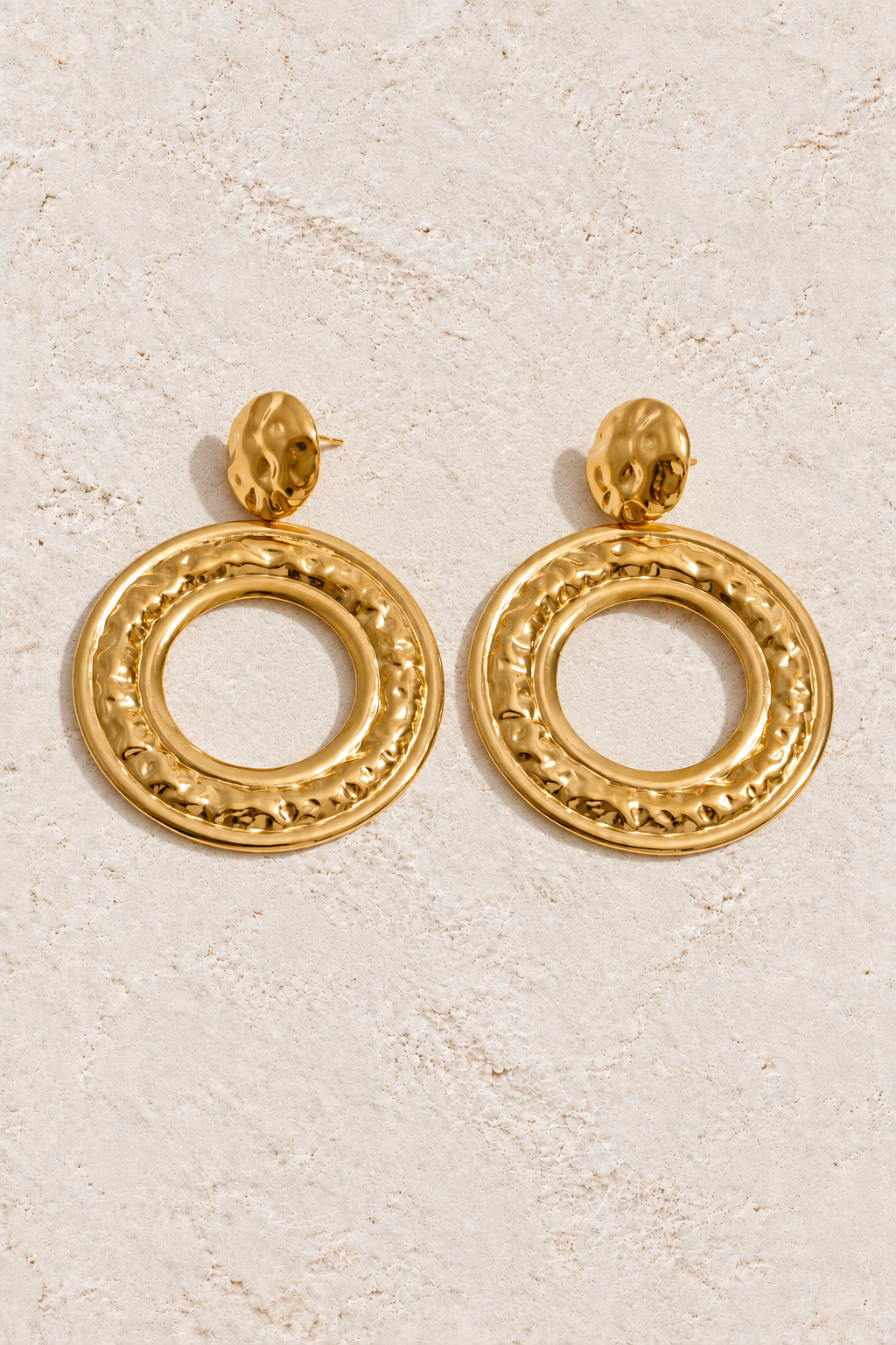 
                  
                    Gold hammered round drop earrings on cream plaster
                  
                