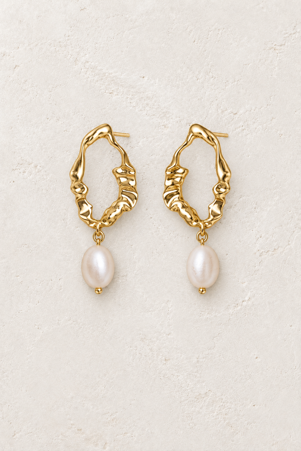 Gold organic link hoop earrings with freshwater pearl drops on a warm off-white textured plaster background