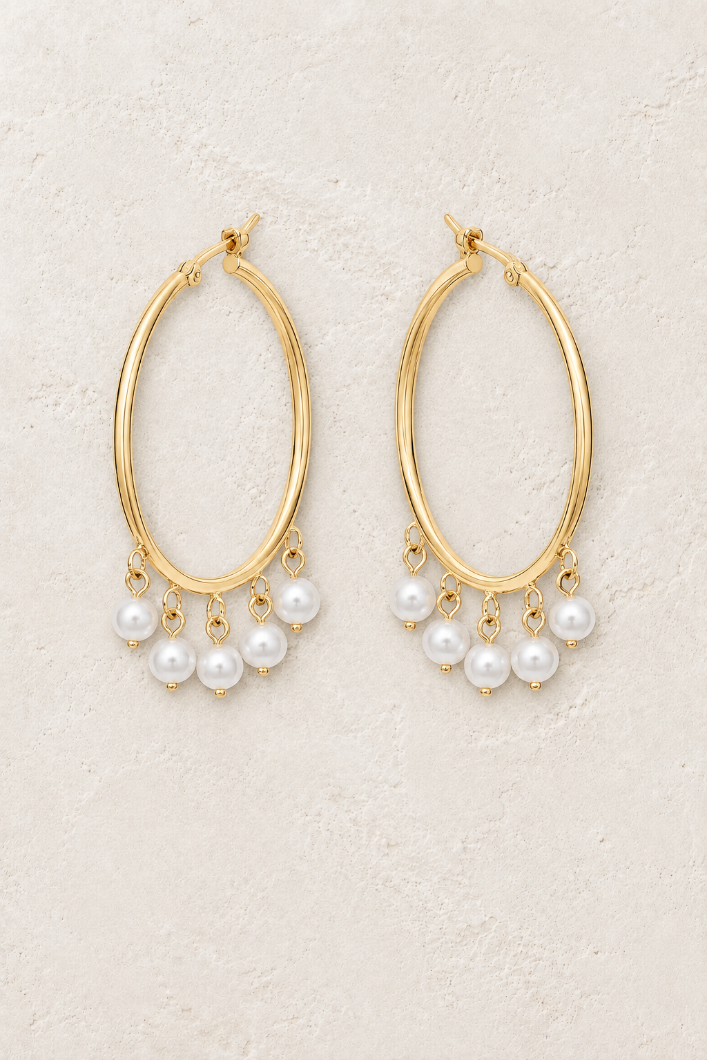 Gold hoop earrings with pearl fringe on a warm off-white textured plaster background