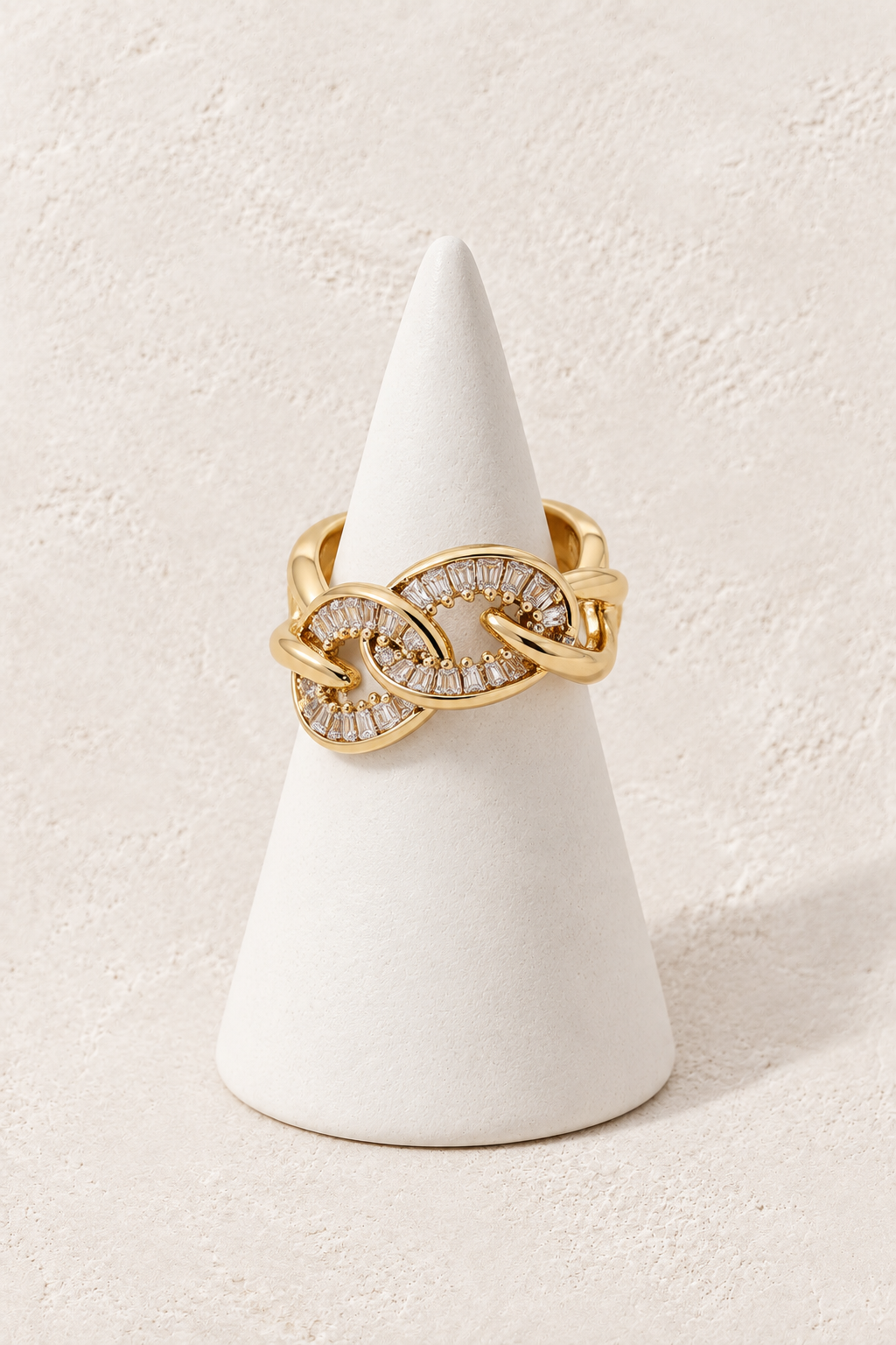 Infinity Luxe Ring on a white display cone against a warm textured background