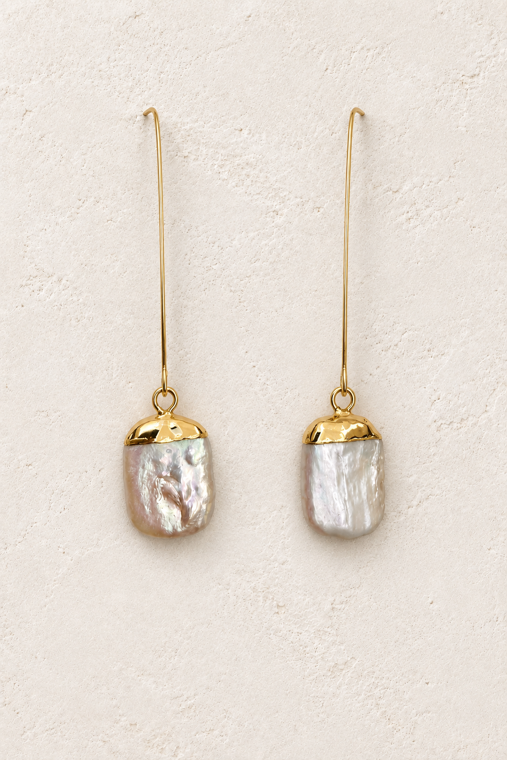 Ione Gold Long Pearl Drop Earrings on cream plaster background