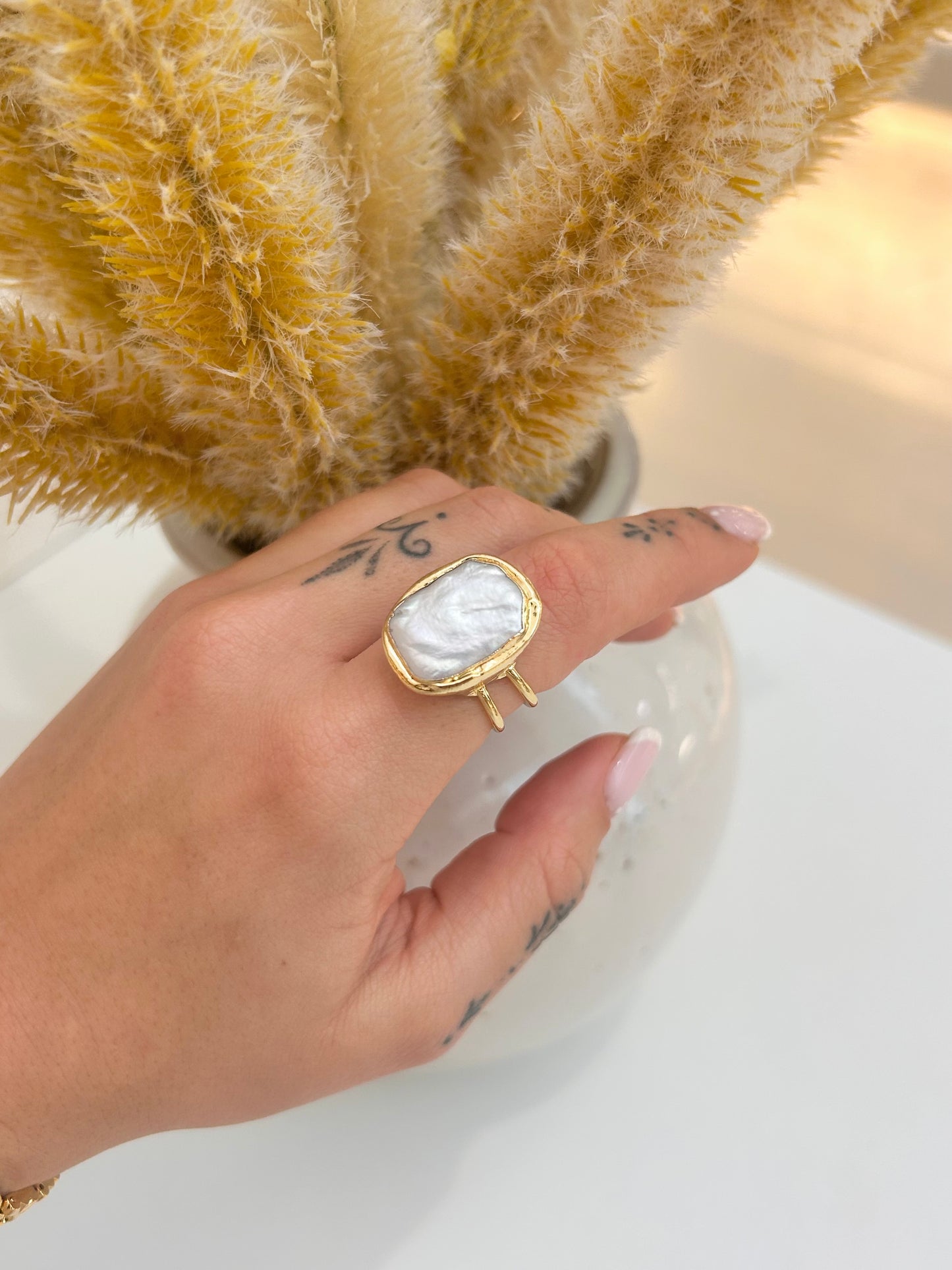 
                  
                    Hand wearing the Isolene Freshwater Pearl Statement Ring featuring a large organic rectangular pearl in a delicate double-band gold-plated design.
                  
                