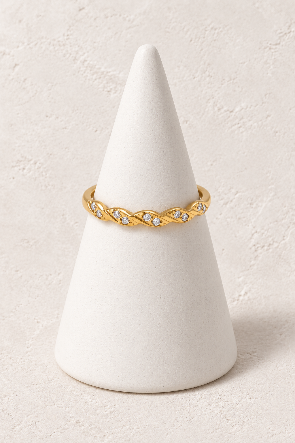 Liora Crystal Braid Ring on a white display cone against a warm textured background