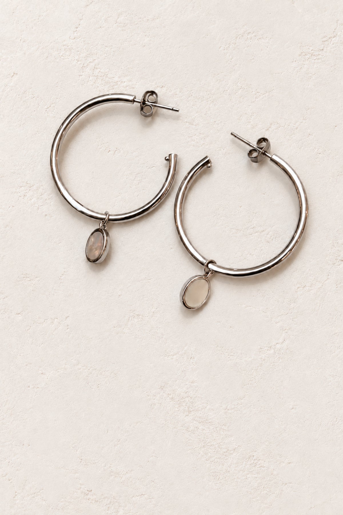
                  
                    Liora silver oval charm hoop earrings on ivory plaster
                  
                