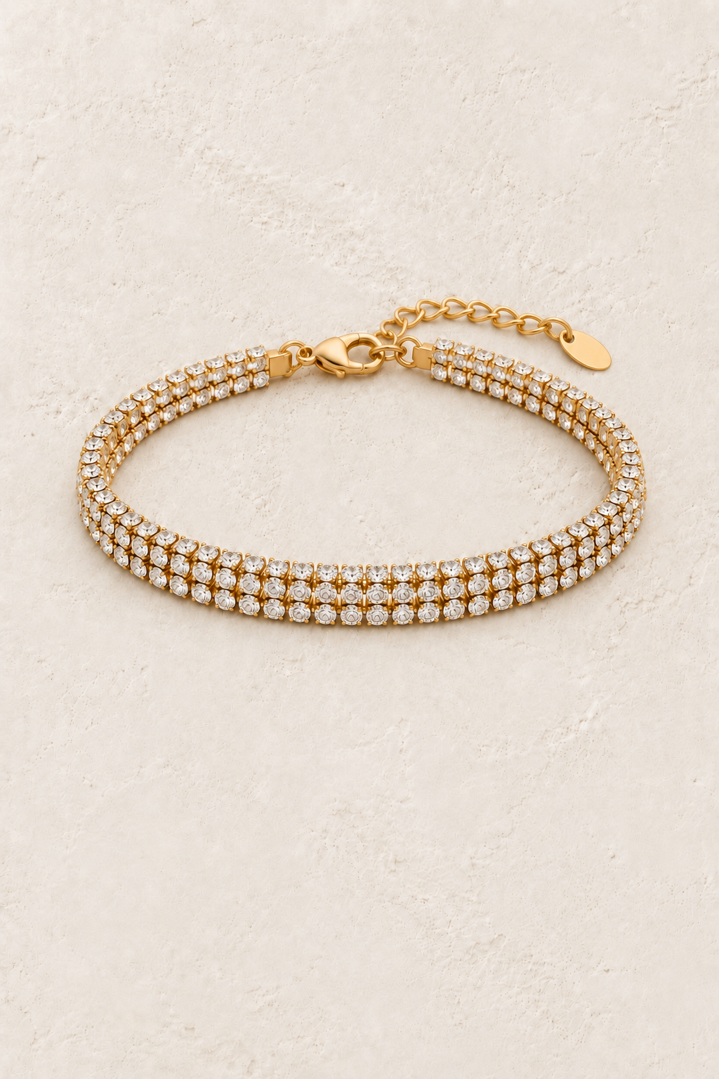 Luciana Gold Triple Row Crystal Tennis Bracelet on a beige textured background