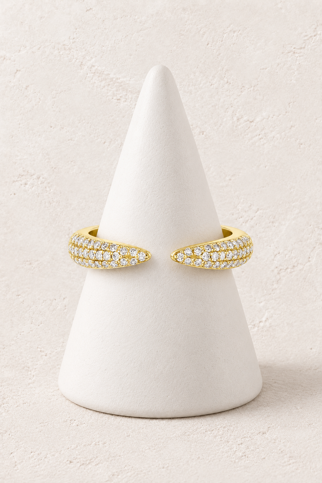 
                  
                    Lumi Pavé Wing Ring on a white display cone against a warm textured background
                  
                