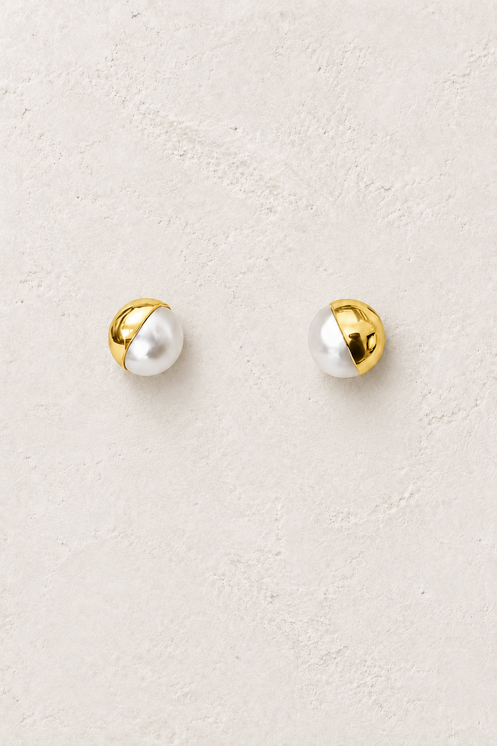 Lumi gold and freshwater pearl stud earrings on a warm textured background