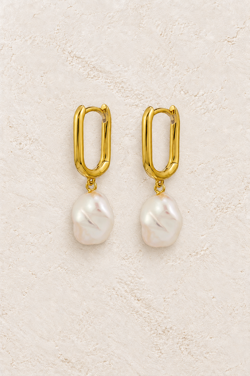 Luna Baroque Pearl Huggie Earrings on warm cream textured background