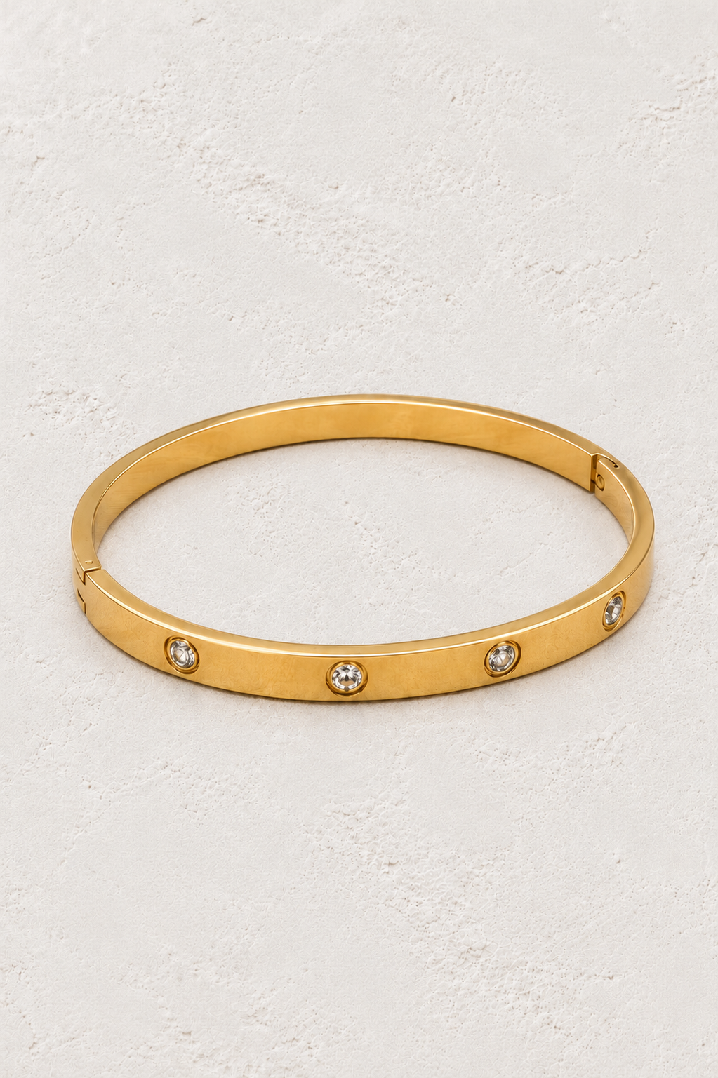 
                  
                    Lunara Gold Crystal Bangle with clear crystal settings on neutral ivory plaster
                  
                