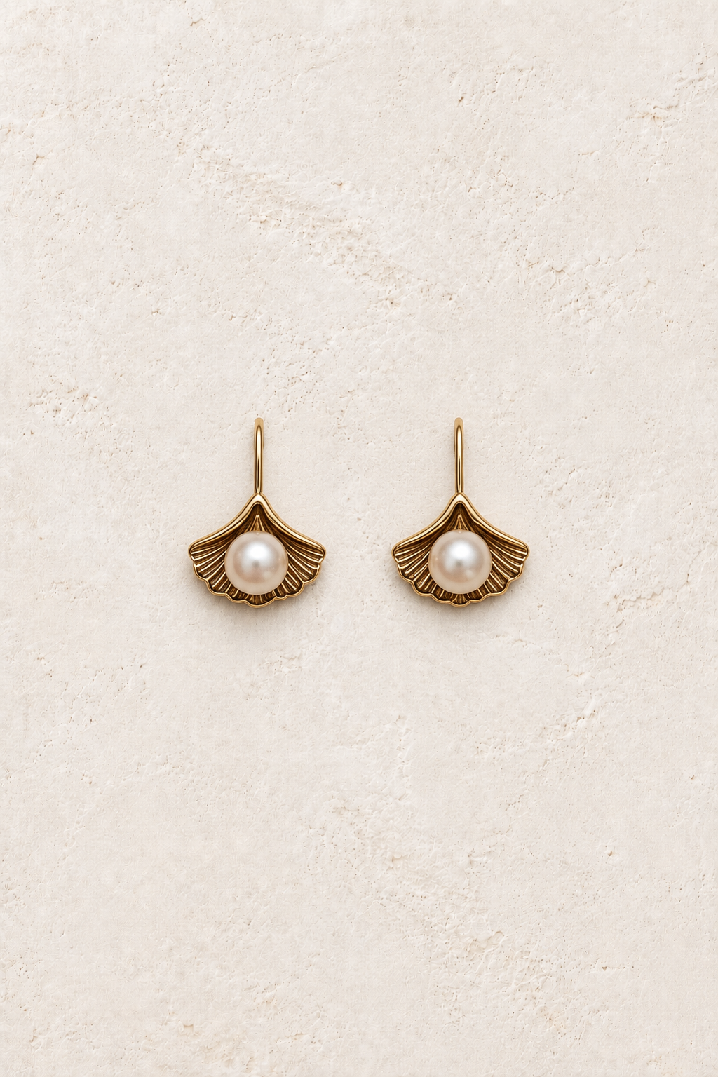 
                  
                    Mira shell fan pearl huggie earrings on warm ivory textured background
                  
                