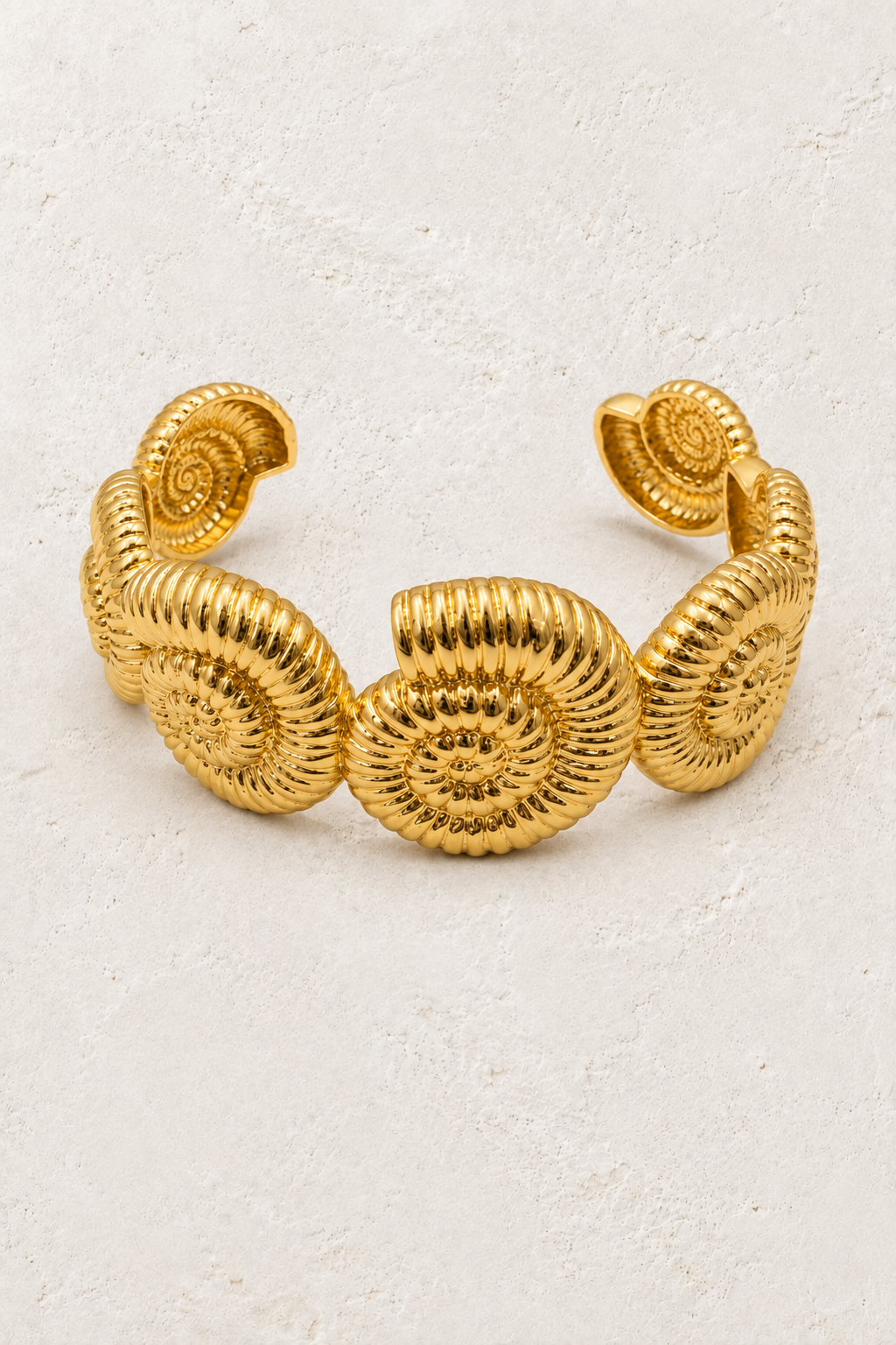Nautila sculptural gold shell statement cuff on a warm off-white textured plaster background