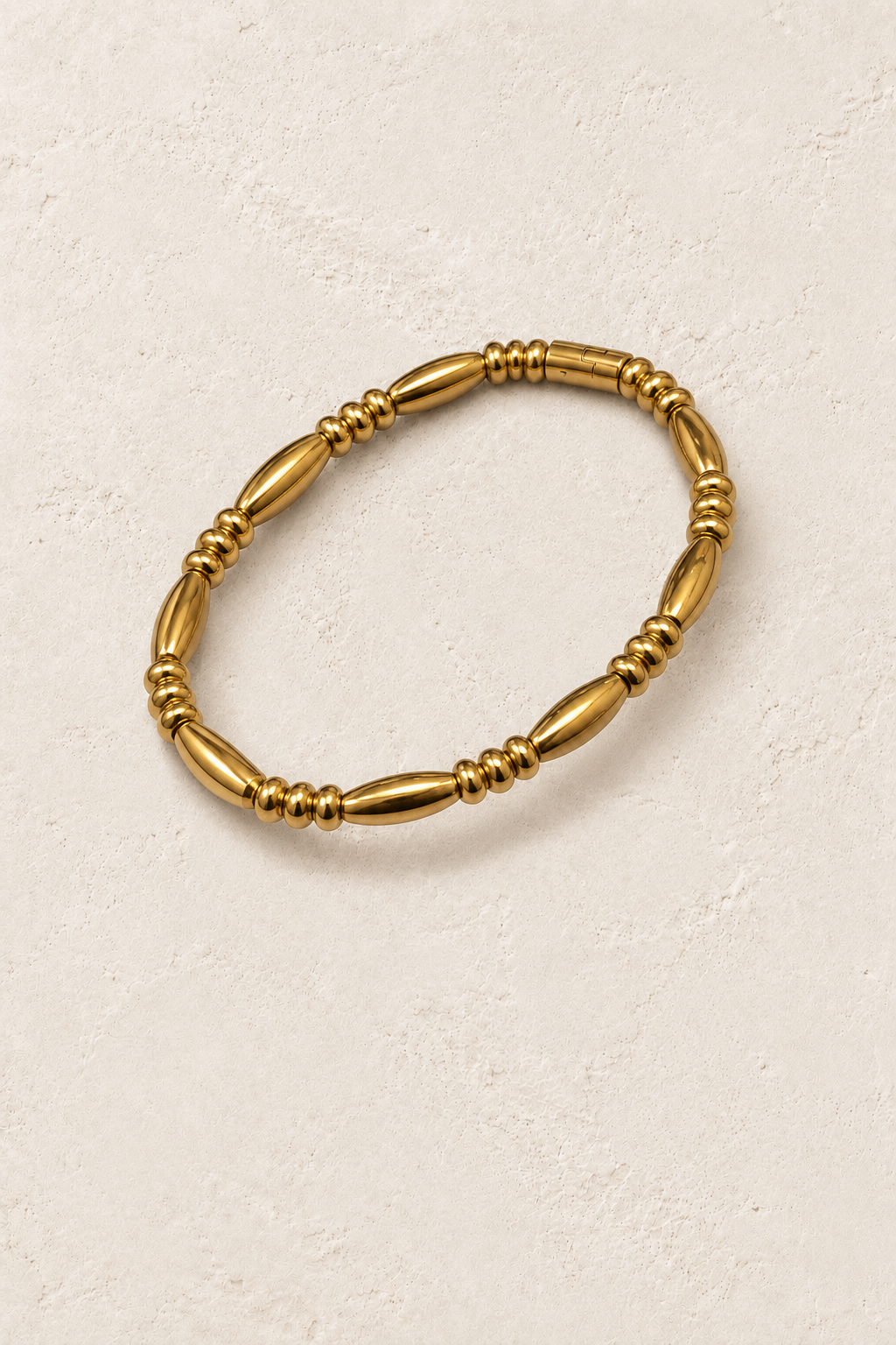 Naya Gold Elongated Bead Bangle on cream beige textured background