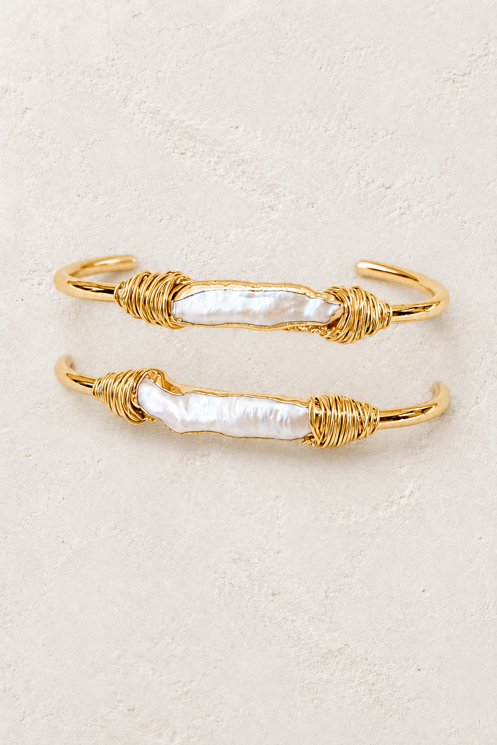 Naya gold cuff with long freshwater pearls on a warm off-white textured plaster background