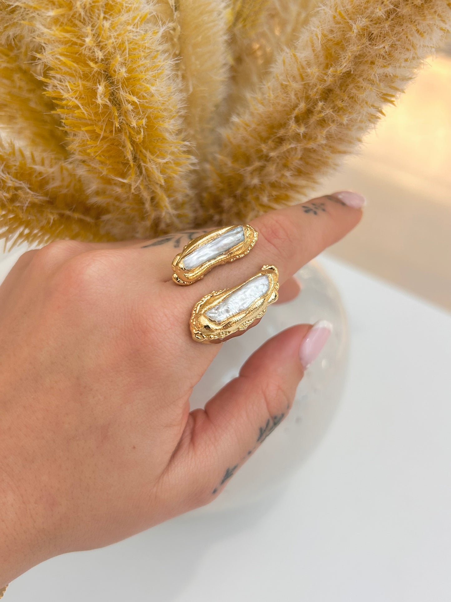 
                  
                    Hand wearing the Nerelle Biwa Pearl Statement Ring featuring two elongated natural freshwater pearls in an open textured gold-plated design.
                  
                