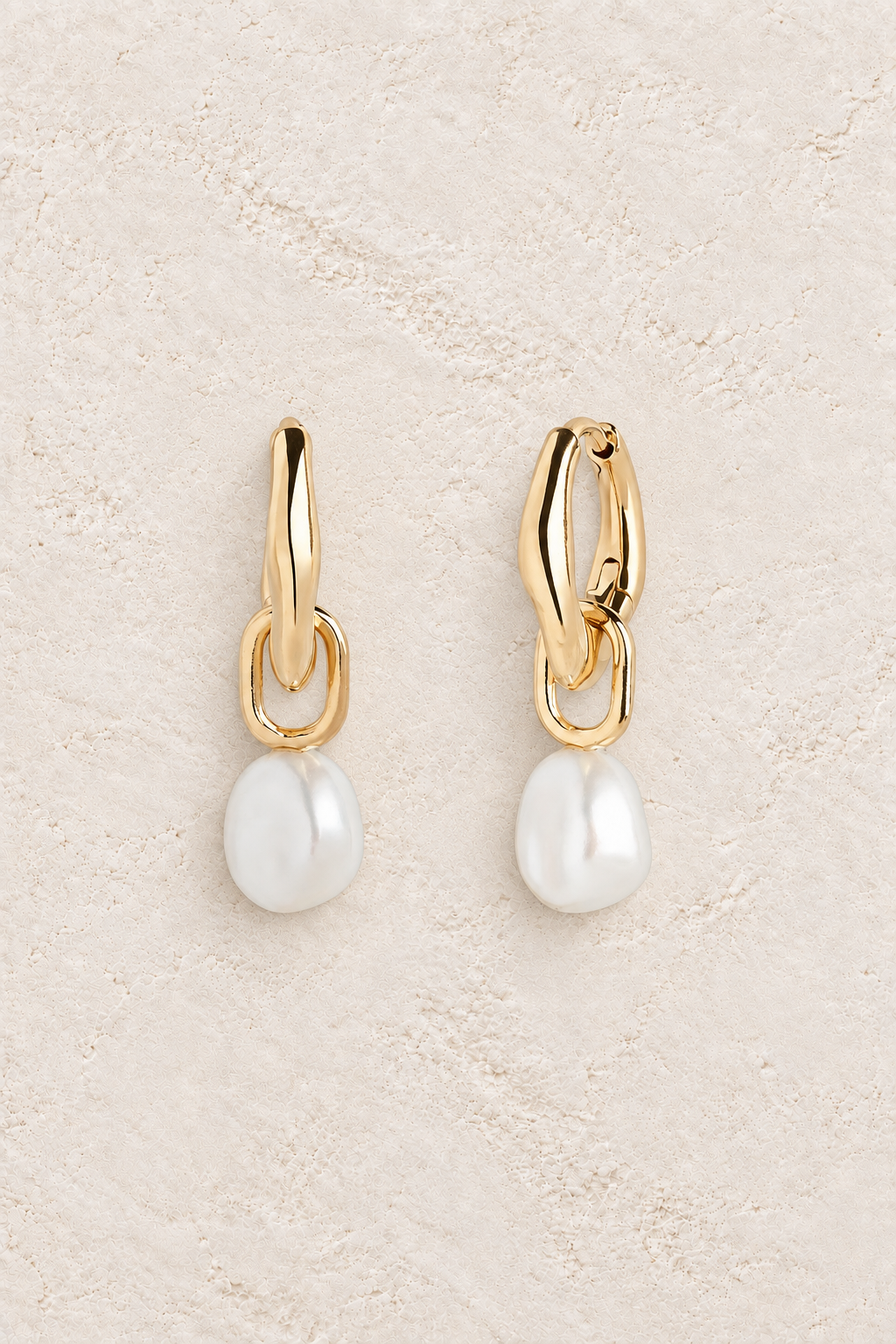 Nina Pearl Link Huggie Earrings on warm cream textured background