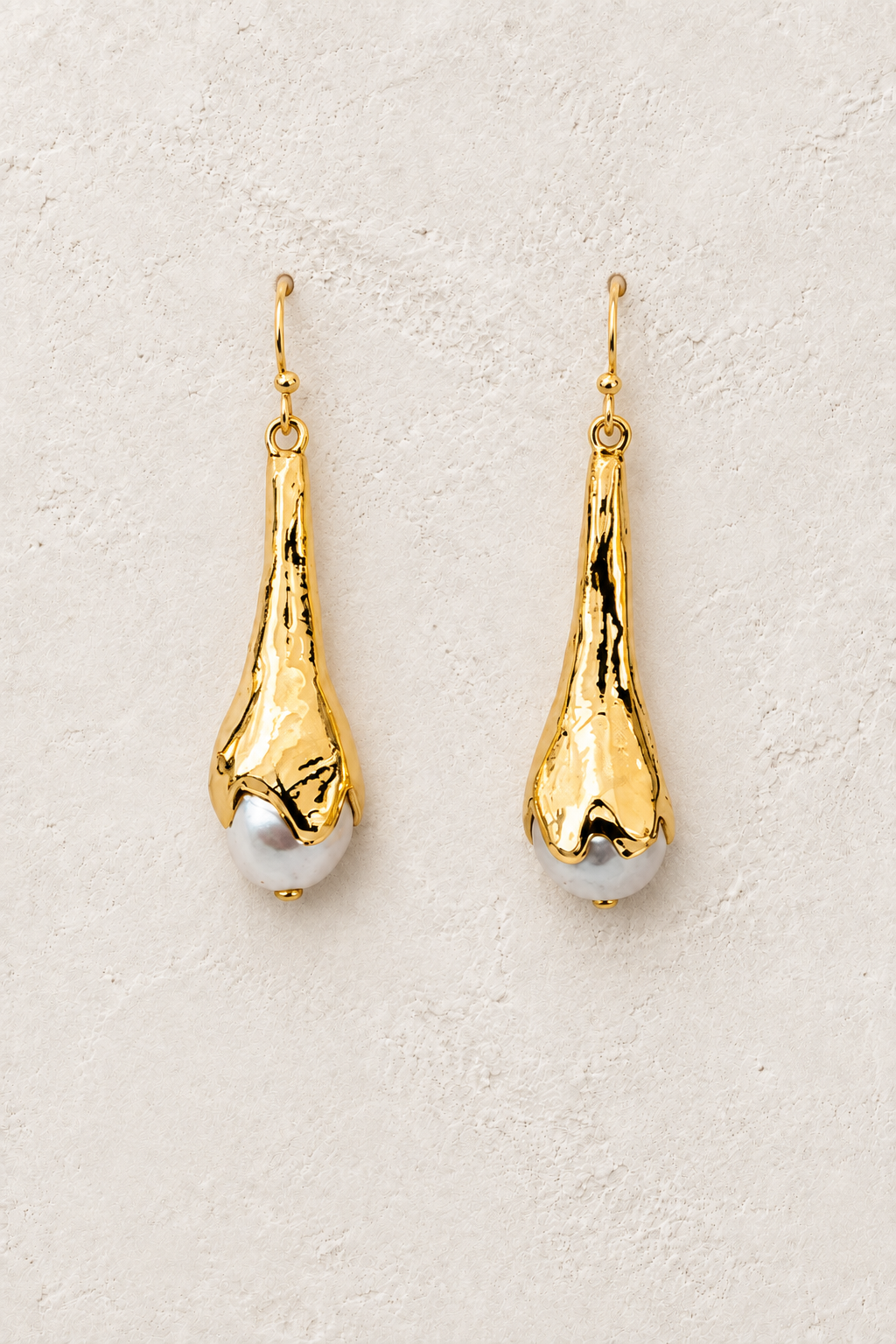 Noelle gold and freshwater pearl drop earrings on a warm textured background