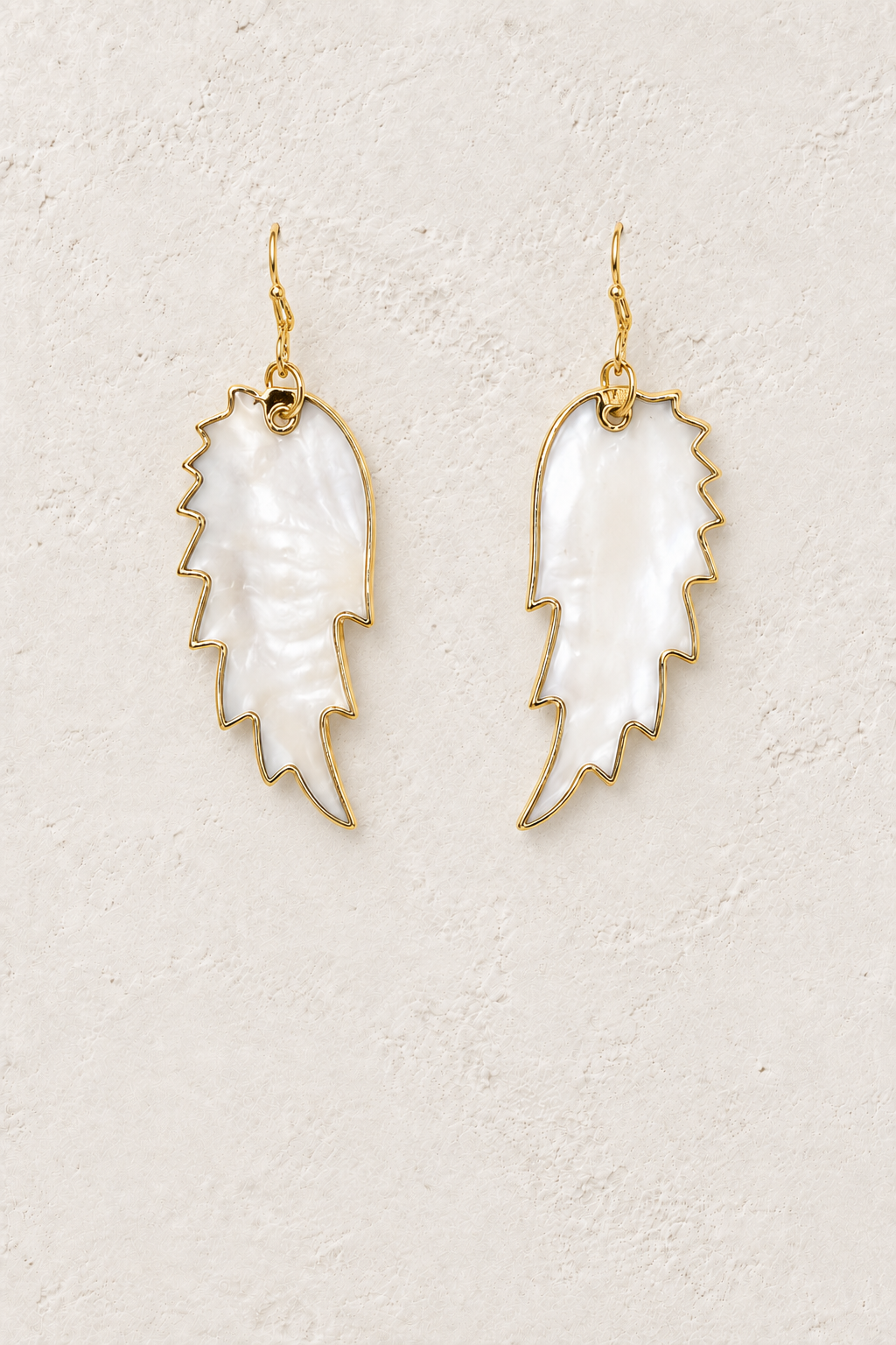 Ocean Feather pearly shell feather drop earrings on a warm off-white textured background