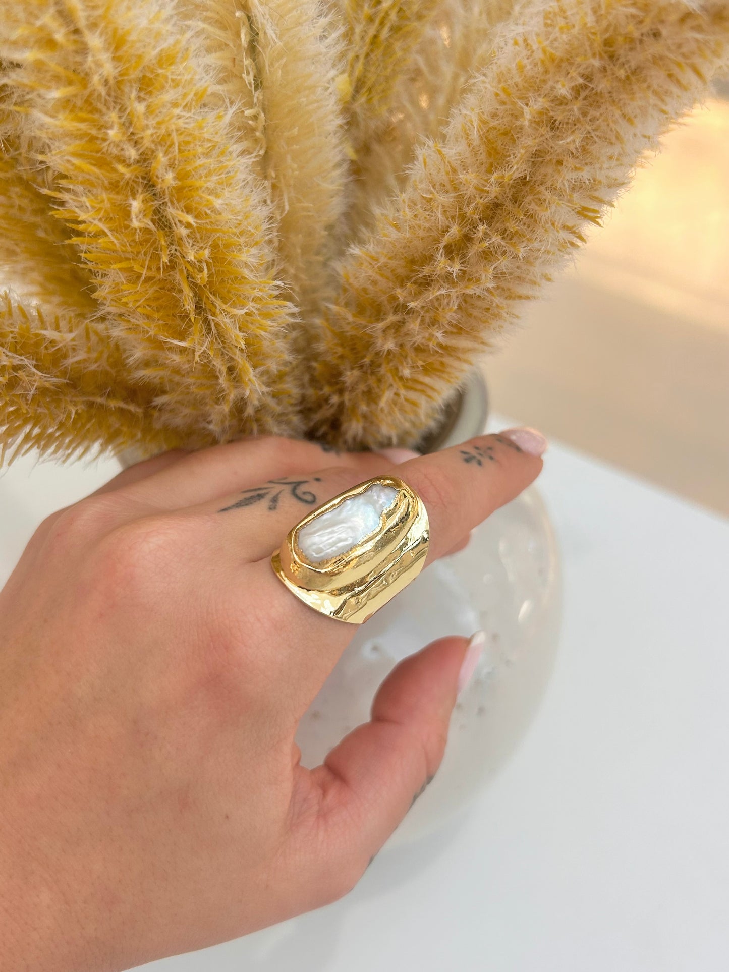 
                  
                    Hand wearing the Ondelle Biwa Pearl Statement Ring featuring a natural elongated pearl and textured gold-plated statement band.
                  
                
