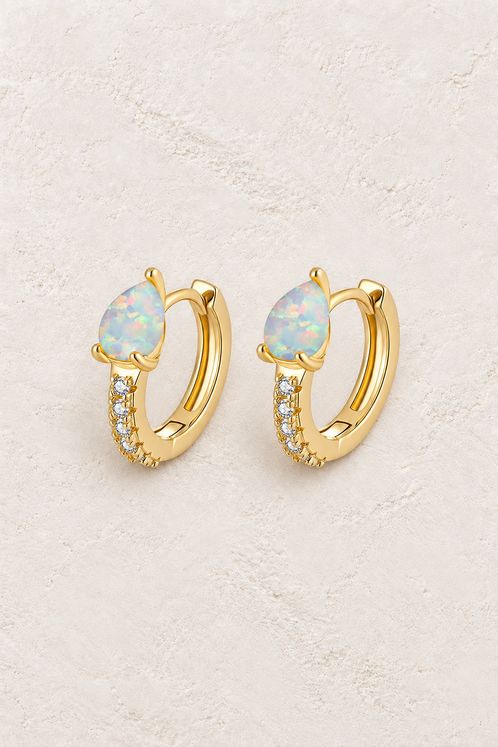 Opal Huggie Hoop Earrings on warm ivory textured background