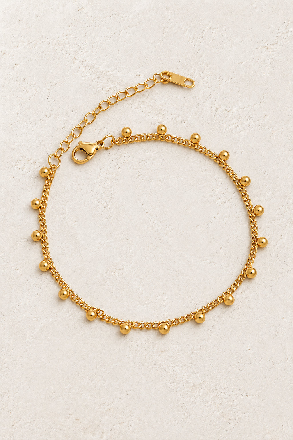 Gold Dangle Bead Bracelet on a beige textured background