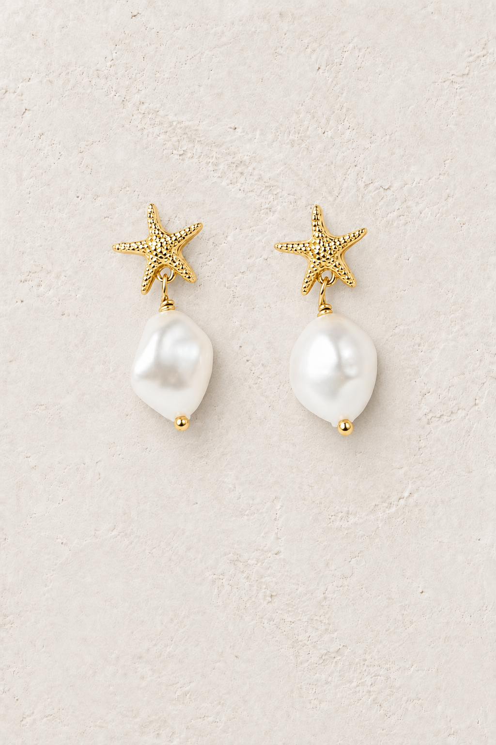 Pearl Estelle freshwater pearl starfish drop earrings on a warm off-white textured background