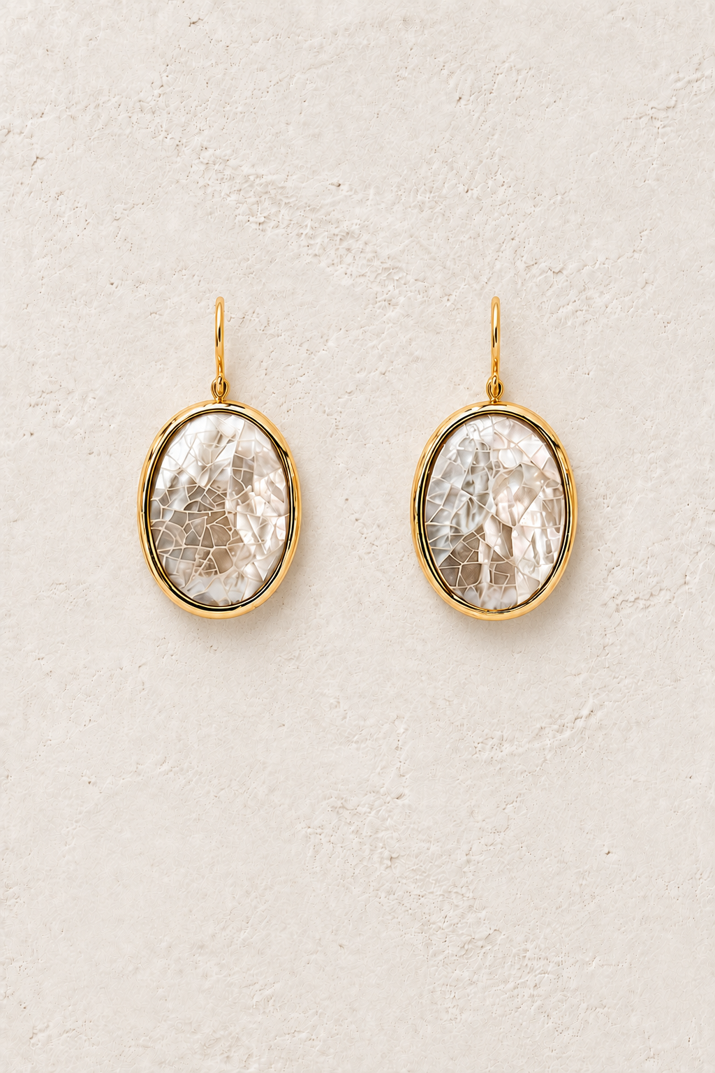 Pearl Halo natural shell oval drop earrings on a warm off-white textured background