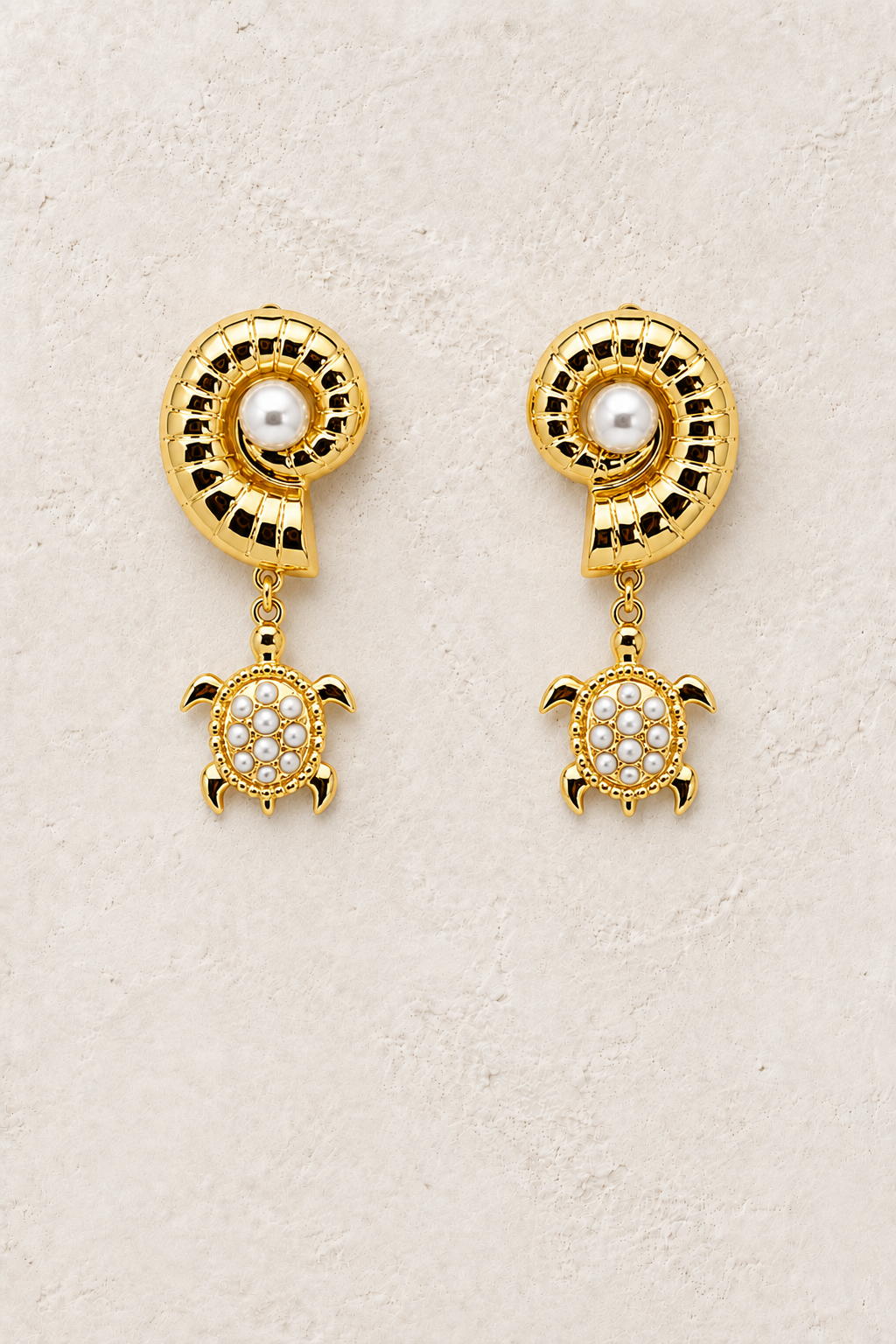 
                  
                    Pearl Marina shell and pearl turtle earrings on a warm textured background
                  
                