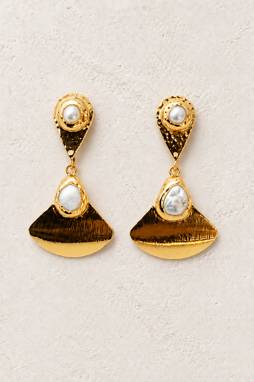 
                  
                    Pearl Mirage gold and freshwater pearl statement earrings on a warm textured background
                  
                