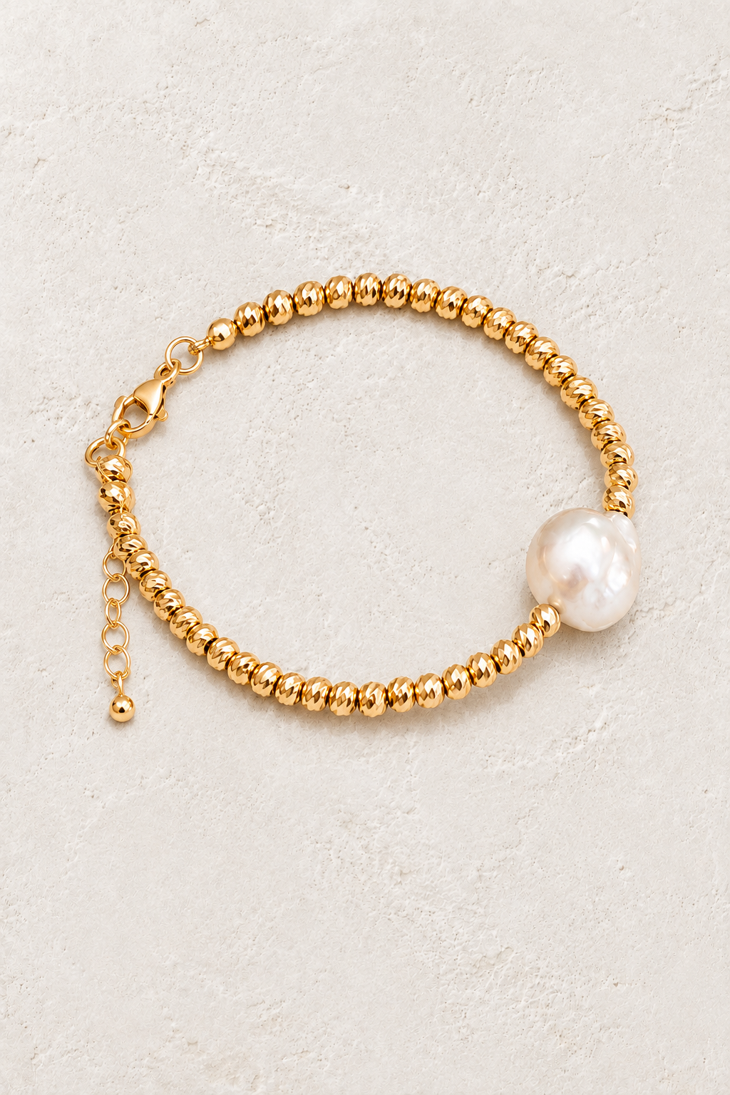 Pearl Muse gold bead bracelet with freshwater pearl accent on a warm off-white textured plaster background