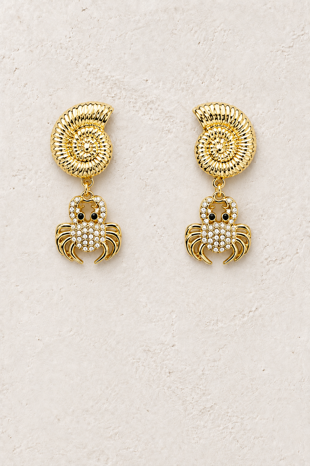 
                  
                    Pearl Nerina shell and crystal crab earrings on a warm textured background
                  
                
