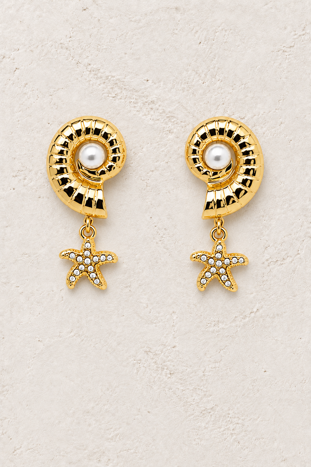 
                  
                    Pearl Oceana shell and crystal starfish earrings on a warm textured background
                  
                