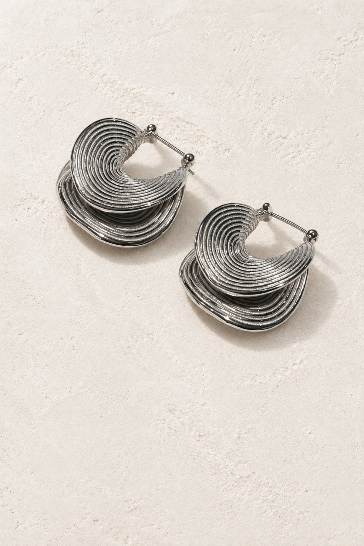
                  
                    Ravena Silver Ripple Hoop Earrings on warm ivory plaster
                  
                