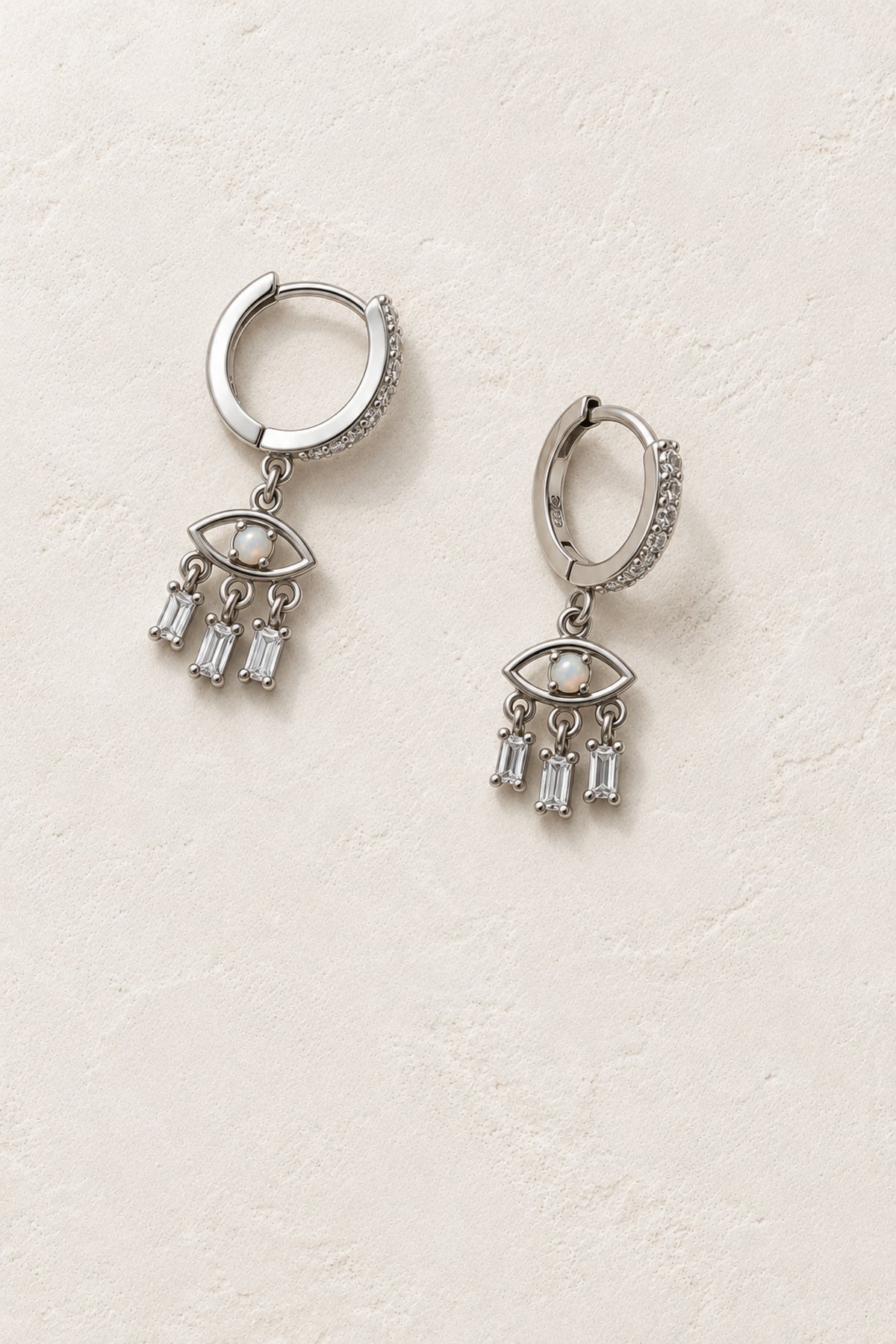 
                  
                    Safira Silver Evil Eye Drop Hoop Earrings - Sterling Silver & Opal on warm ivory plaster
                  
                