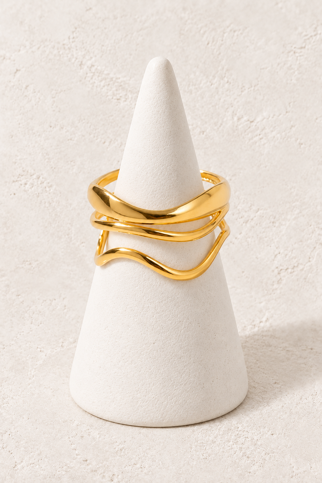 
                  
                    Sculpted Wave Gold Ring on a white display cone against a warm textured background
                  
                