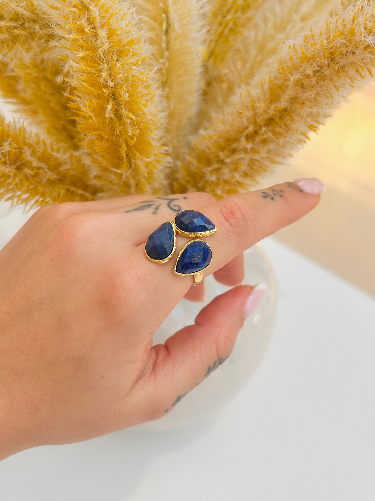
                  
                    Hand wearing the Seraphine Lapis Lazuli Statement Ring by Boho & Mala featuring three natural deep-blue gemstones.
                  
                