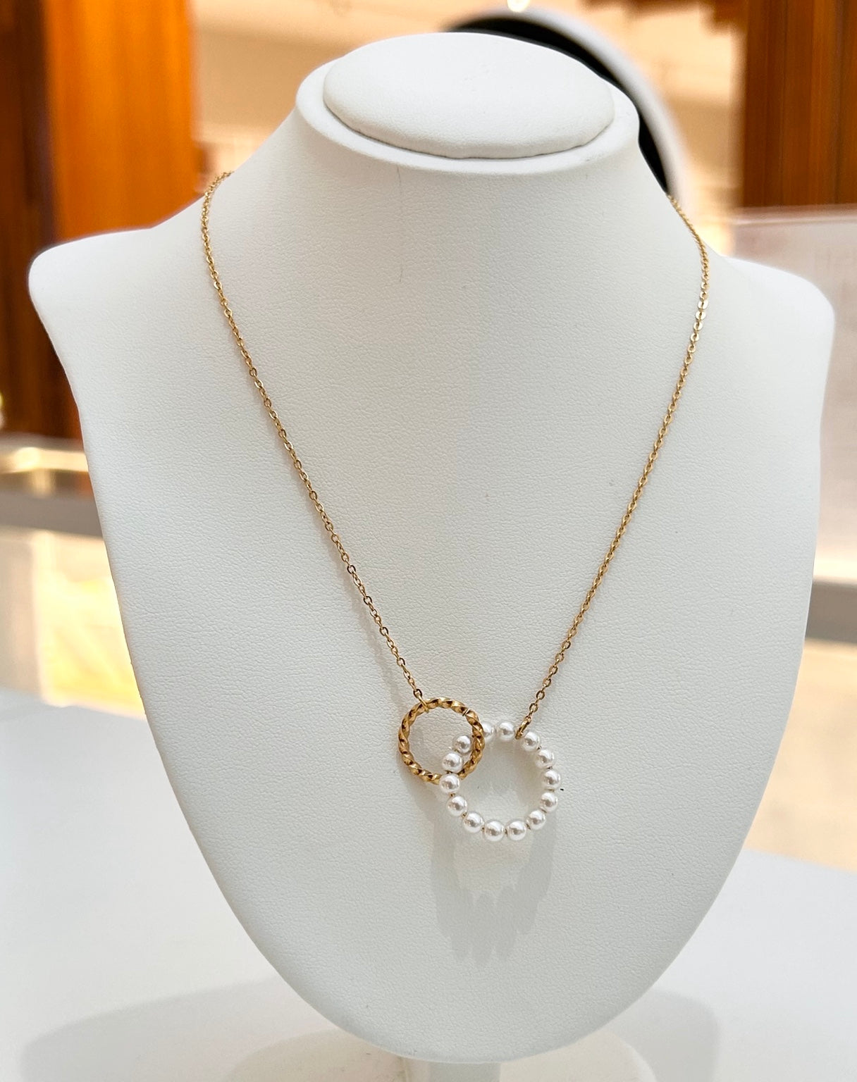 
                  
                    Serenelle pearl and textured gold circle necklace displayed on a jewellery bust
                  
                