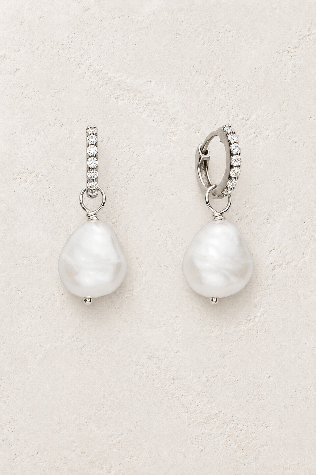 Sterling silver crystal huggie earrings with baroque pearl drops on a warm off-white textured plaster background
