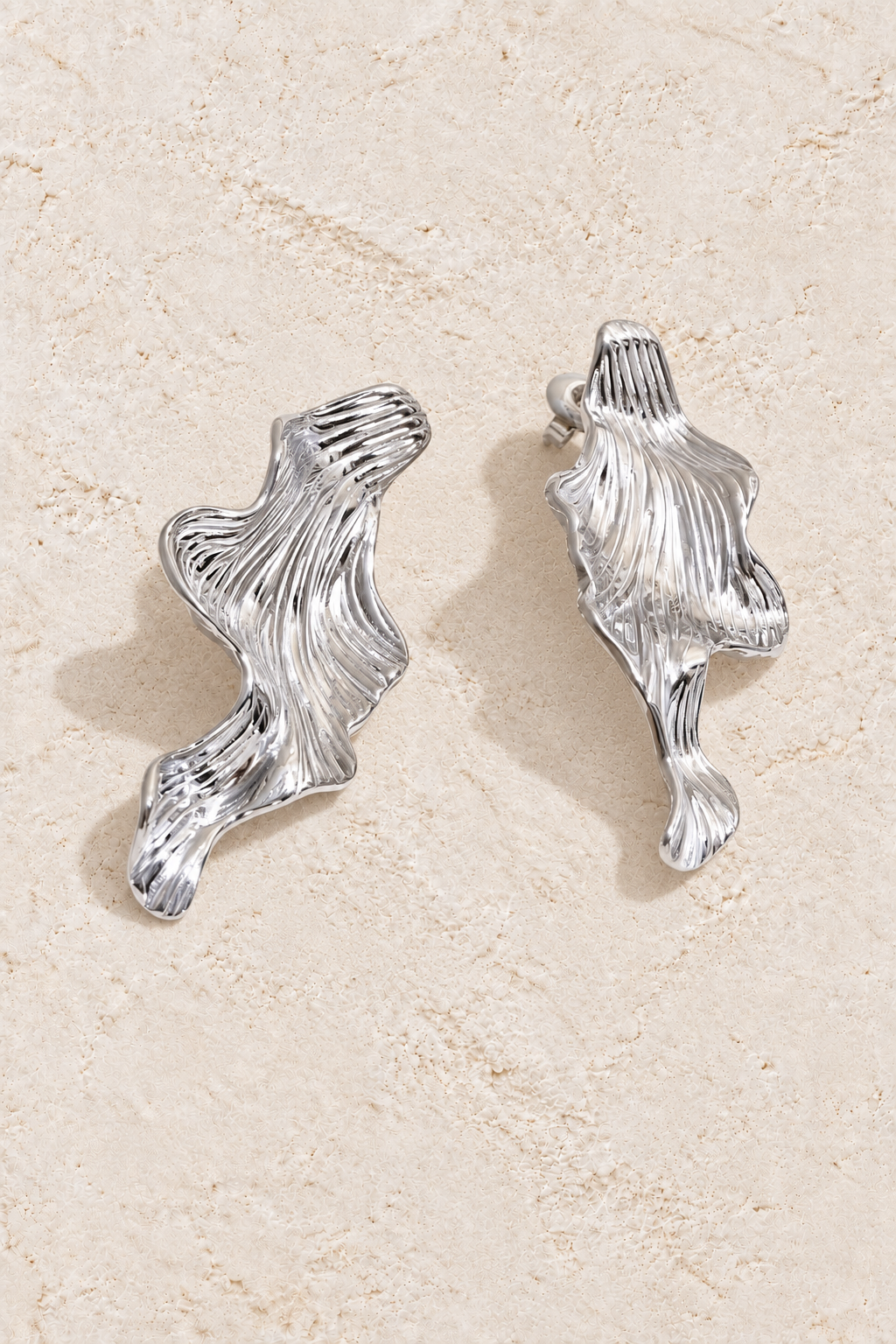 silver sculptural ridged wave earrings on cream plaster